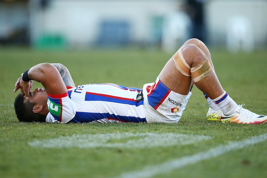 A man slumps on the ground after losing an NRL match 
