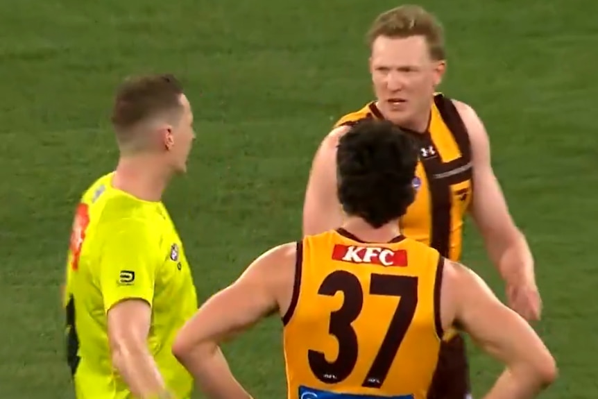 A pair of AFL players exchange words with an umpire during a game.