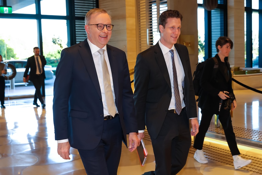 Two smiling men in dark suits walk through a foyer.