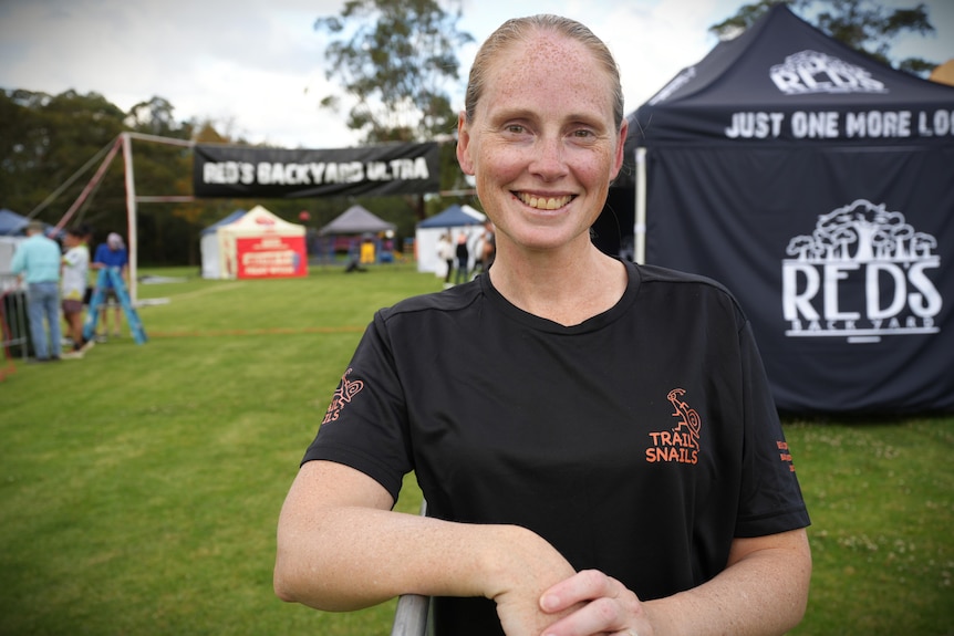 Woman with strawberry blonde hair, wearing black shirt in front of race start line