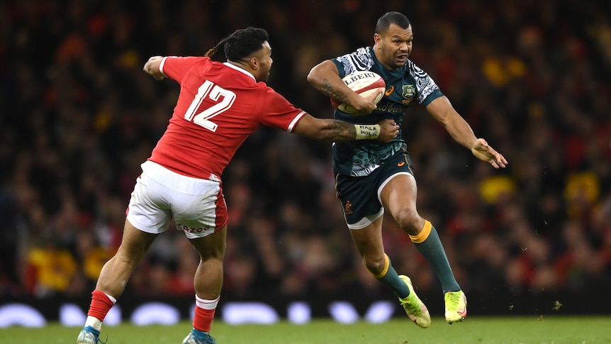 Wallabies player Kurtley Beale tries to twist his body as he runs to evade a Welsh tackle.