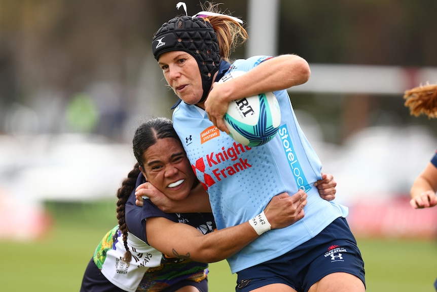 Emily Chancellor of the Waratahs runs with the ball as she is tackled by a Brumbies opponent.
