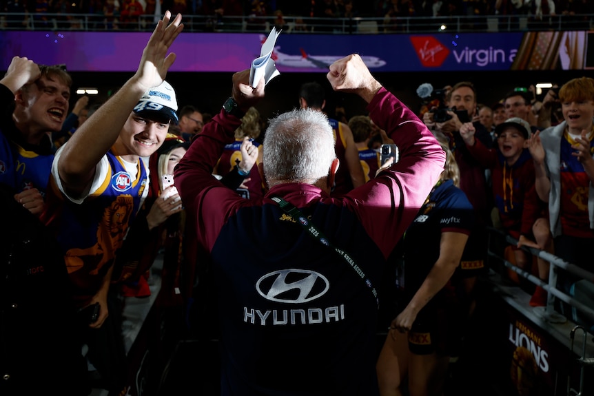 chris fagan is swarmed by brisbane lions fans and pumps his fists in the air in celebration