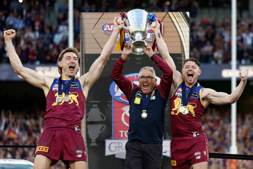 Harris Andrews, Chris Fagan and Lachie Neale hold up the AFL premiership trophy.