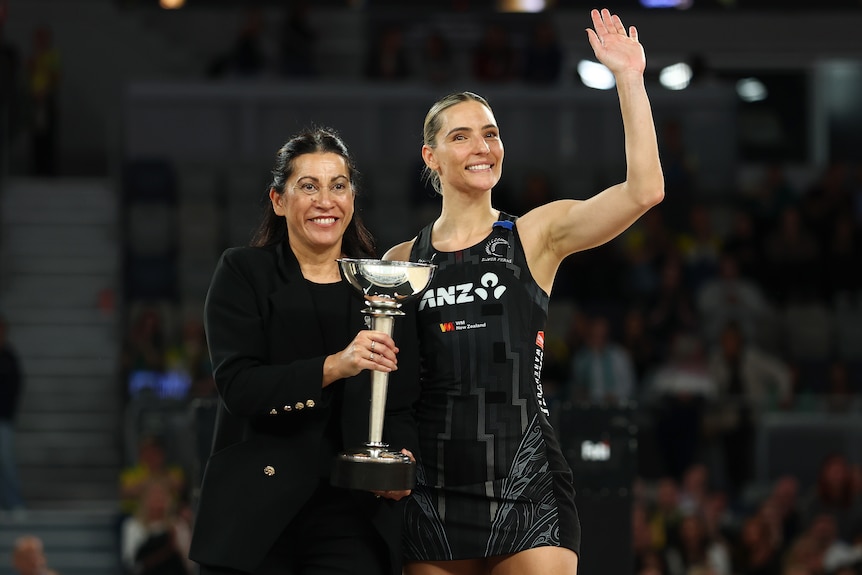 A coach and player smile and wave to the crowd as they pose with a trophy