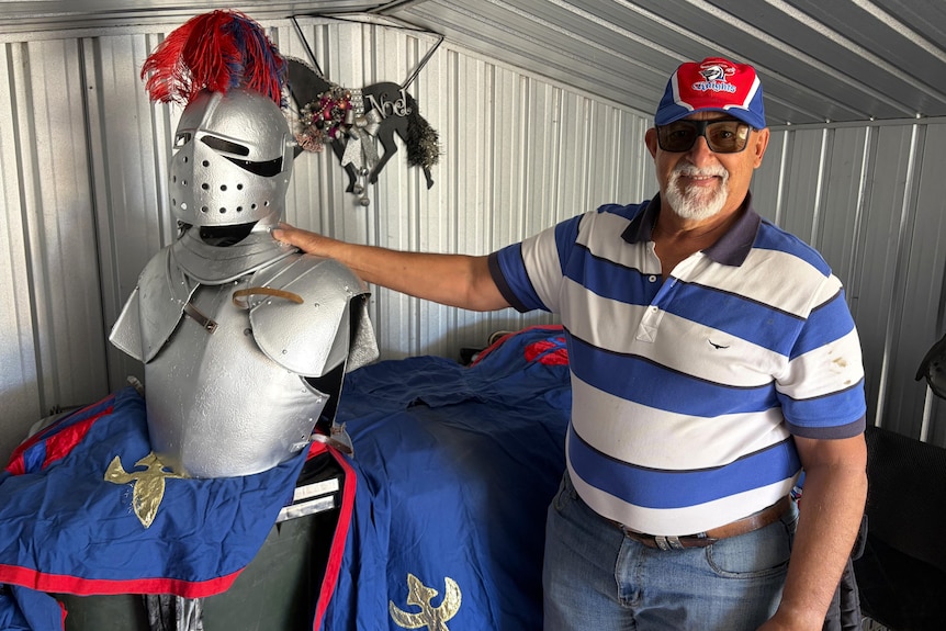 A man in a blue-and-white striped shirt rests a hand on a suit of armour.
