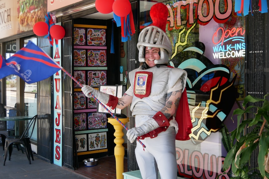 A man dressed up in a suit of armour made of fabric and holding a Knights flag.