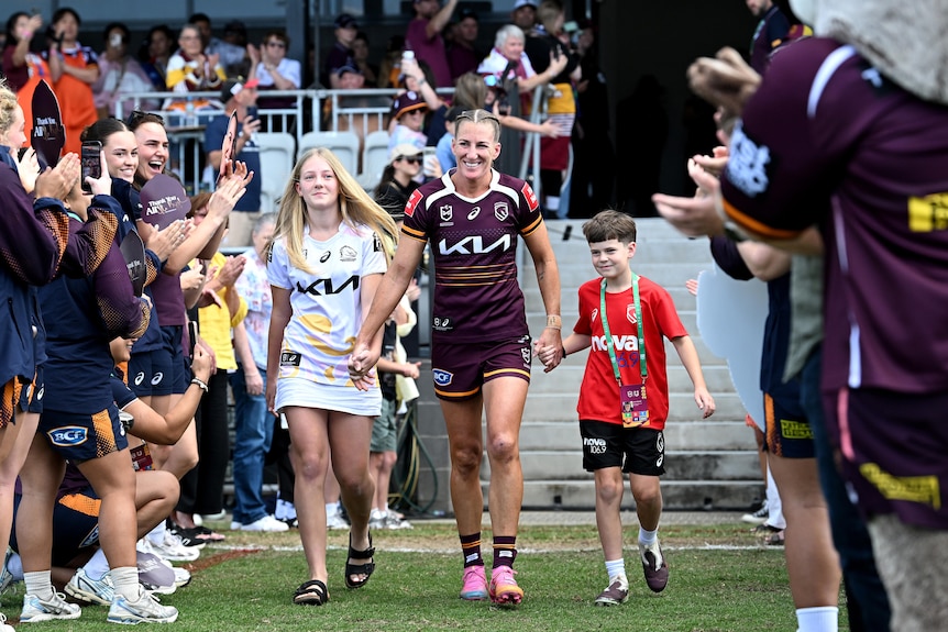 Ali Brigginshaw walks out, holding the hands of two children with players either side
