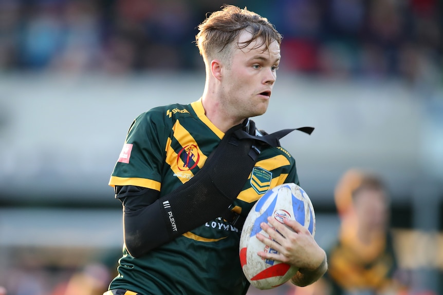 A male physical disability rugby league player carries the ball in his left arm, his right is wrapped in a black sleeve s