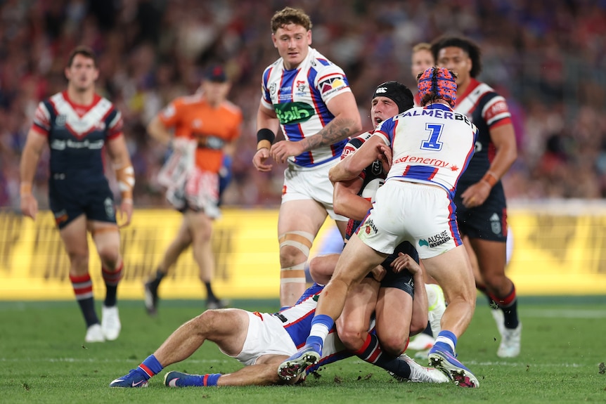 A rugby league player in blue and white shoulder charges a player in red and blue
