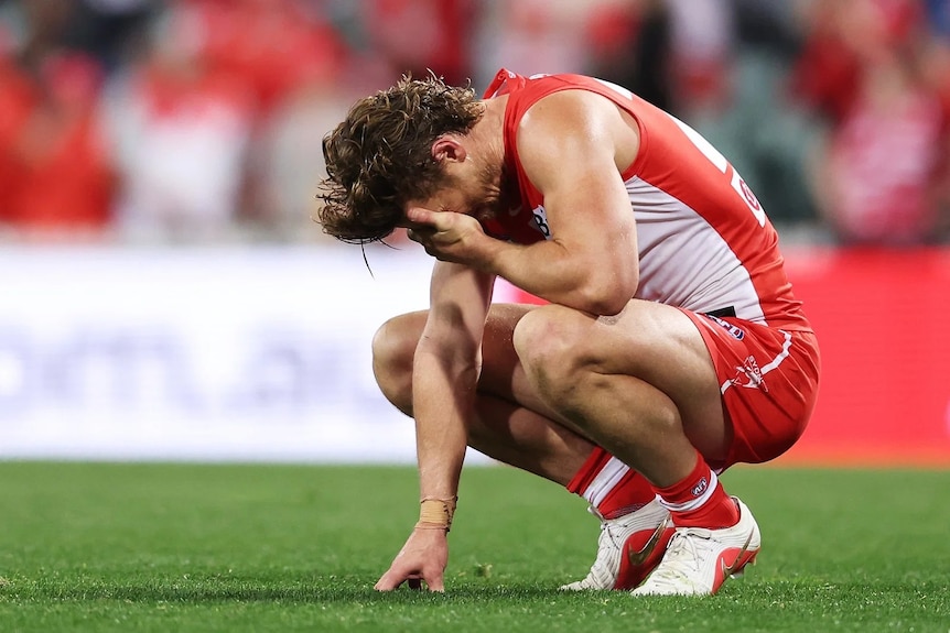 Dane Rampe of the Swans on his haunches, holding his head, crying on the field.