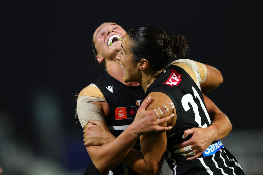 Two AFLW players in black and white embrace and celebrate a victory