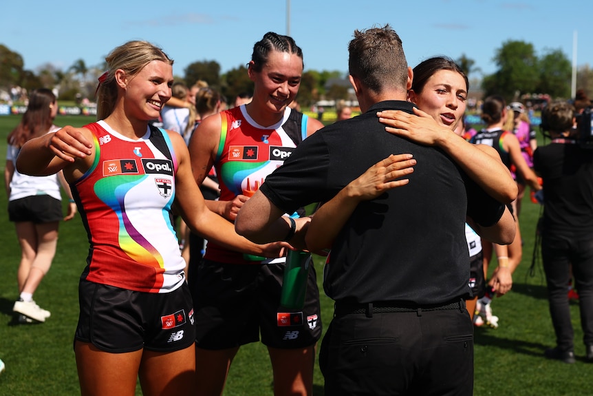 A group of AFLW players embrace their coach after the match 