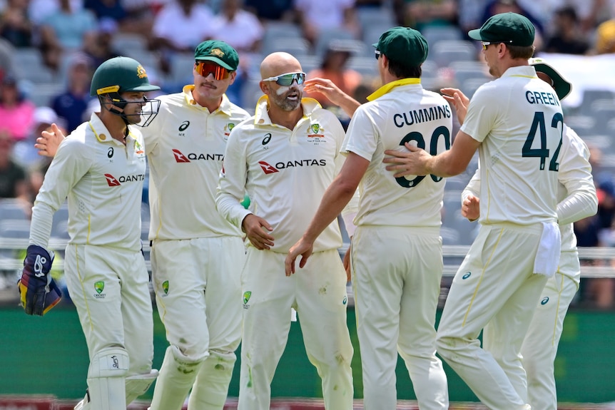 A group of cricketers gather in celebration of a wicket