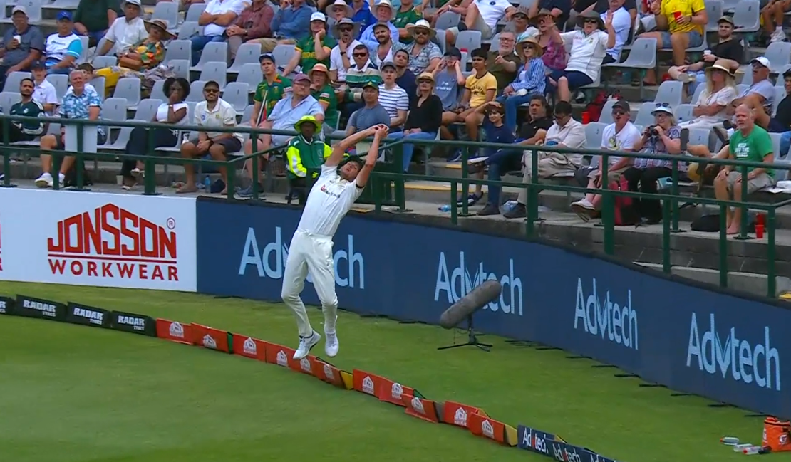 A cricketer takes an overhead catch on the boundary
