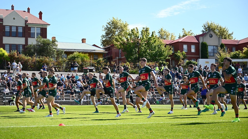 Athletes warming up in formation on grass at sporting oval.