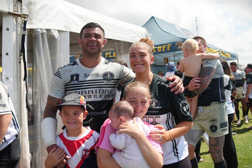 A man and women in rugby league jerseys hugging their children.