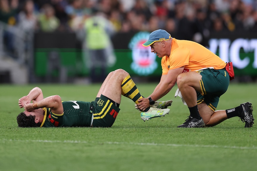 Rugby league player lays on the ground, a medic treats his leg